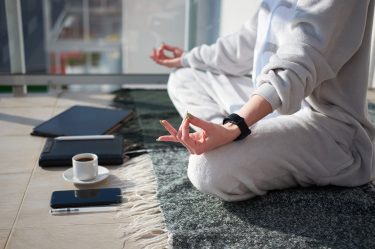 Mulher branca meditando na varanda em pijama antes de trabalhar, com tablet e celular